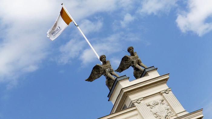 Två statyer och en flagga på toppen av en vit byggnad.